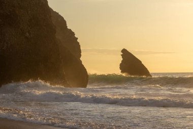 Altın gün batımı Adraga sahilindeki kayalara çarpan dalgaları aydınlatıyor, sintra, Portekiz