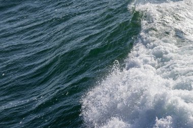 Koyu mavi bir okyanus dalgasının yüzeyinde beyaz deniz köpüğü oluşuyor.