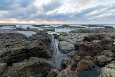 Güneş bulutların arasından parlıyor kayalık kıyı şeridini aydınlatıyor ve Sintra, Portekiz 'deki Magoito sahilinde gel-git havuzları var.