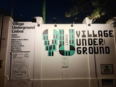 Köyün yeraltı logosu ve tabelalarının yer aldığı duvar, gece aydınlatılmış, kentsel sanat ve kültürel sunumları vurguluyor.