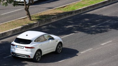 Modern beyaz jaguar ve şehir ortamında asfalt yolda hız yapıyor.
