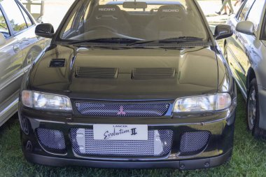 Siyah Mitsubishi Lancer II 'nin ön görüntüsü çimlerin üzerine park edilmiş, sportif tasarımı ve güçlü özellikleri vurgulanıyor.