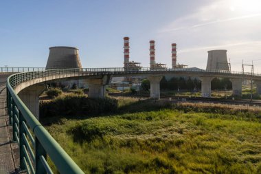 Portekiz 'deki Ribatejo termoelektrik santralinin manzarası, bacalar, soğutma kuleleri, yükseltilmiş bir yol ve demiryolu rayları.