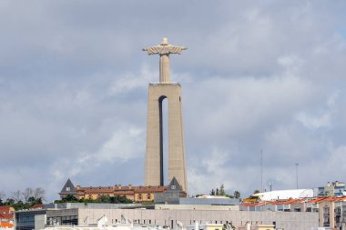 Cristo Rei heykeli, arka planda bulutlu bir gökyüzü olan Portekiz 'in Almada kentinin üzerinde dik duruyor.