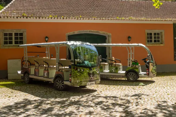 Tapada Nacional de Mafra, Portekiz 'de turuncu bir binanın önüne park edilmiş iki elektrikli servis otobüsü sürdürülebilir ulaşım imkanı sunuyor.