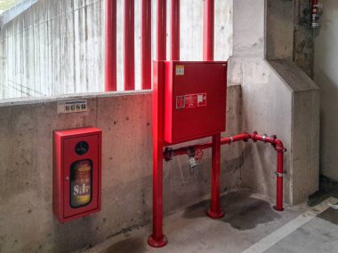 Kırmızı yangın söndürme ekipmanları, yangın söndürücü, borular ve içerideki beton bir binayı koruyan vanalar.