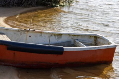 Küçük turuncu tekne yavaşça bir gölün kumlu kenarında dinleniyor.
