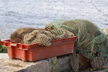 Balık ağları suyun yakınındaki turuncu plastik bir sandıkta kuruyor.