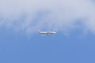 Mavi gökyüzünde, bulutlarla birlikte uçan beyaz yolcu uçağı