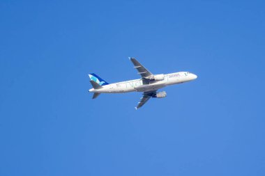 Modern jet uçağı, uluslararası seyahat ve bağlantıyı sembolize eden, parlak mavi gökyüzünün engin genişliğinde süzülüyor.