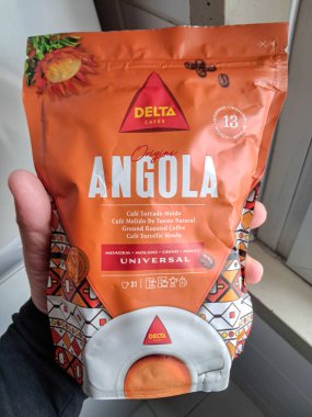 Elinde bir çanta dolusu Angola kahvesi, kavrulmuş kahve, canlı ambalaj ve ürün detaylarını gösteren biri.