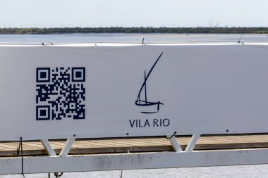 Povoa de Santa Iia, Portekiz 'deki tagus nehrinin yanında yer alan vila rio için QR kodu ve yelkenli logosu gösteren beyaz tabela.