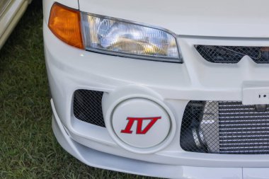 Beyaz Mitsubishi Lancer IV 'ün ön tampon, far ve sis ışığı kapağının detaylı görüntüsü çimenlere park edilmiş.