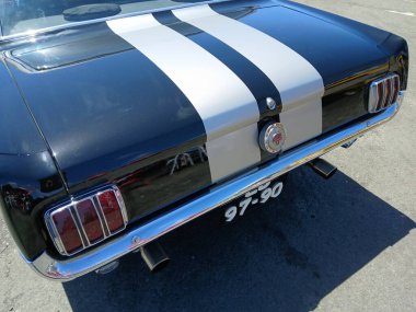 Parlak siyah bir Ford Mustang 'in arkasında asfalta park edilmiş gümüş yarış çizgileri var.