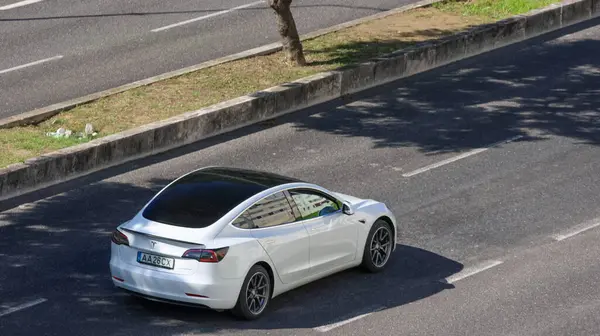 Kentsel çevrede asfalt yolda giden beyaz tesla modeli 3 elektrikli araba, sürdürülebilir ulaşımı temsil ediyor