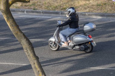 İş kadını, asfalt yolda, ağaç gövdesinin yanında, hava manzaralı modern scooter kullanıyor.