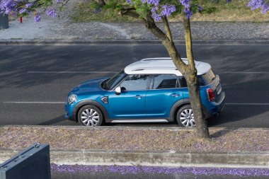 Modern mavi küçük vatandaş asfalt bir yolda, çiçekli bir Jacaranda ağacının altında, hava manzaralı...