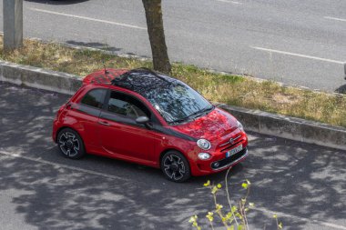 Güneşli bir günde yol kenarında siyah çatı parkı olan kırmızı bir Fiat 500 'ün hava görüntüsü.
