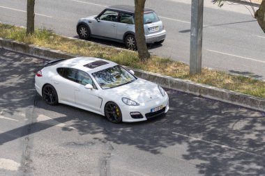 Beyaz Porsche Panamera yol kenarına park ederken mini Cooper güneşli bir yaz gününde sokakta araba sürüyor.