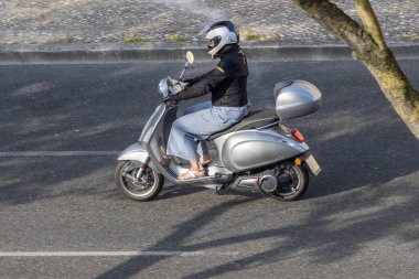 Şehir yolunda gri Vespa Elettrica scooter kullanan bir kadın.