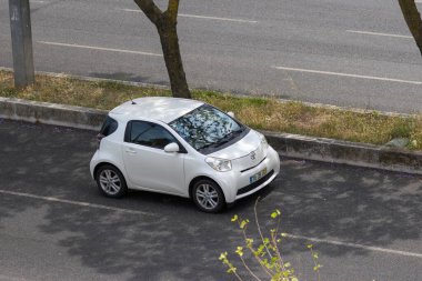 Yoğun bir yolun kenarına park edilmiş beyaz Toyota Iq, yukarıdan görülmüş.