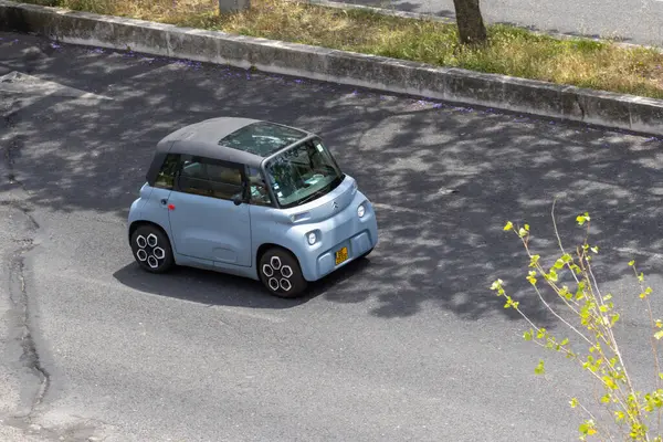 Açık mavi citroen ami, küçük elektrikli bir araba, kaldırımlı bir yolda sürüyor, yukarıdan görünüyor.