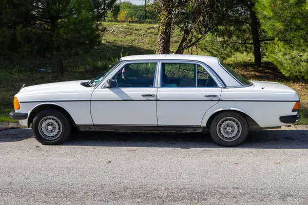 Klasik beyaz Mercedes Benz w123 sedan. Asfaltta, ağaçların yanında park edilmiş.