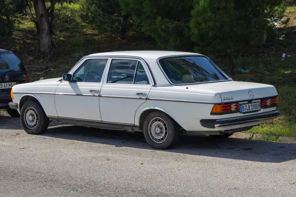Klasik beyaz Mercedes Benz W123 yol kenarına park etmiş, klasik tasarımını sergiliyor.