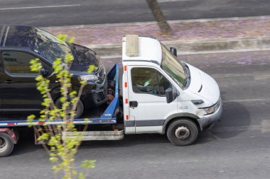 Çekici yolda bozuk siyah bir minibüs taşıyor.