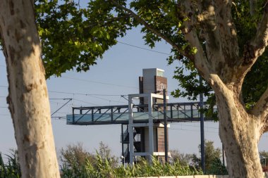 Modern cam ve çelik yaya köprüsü Villada tren raylarından geçiyor franca de xira, Portekiz, ağaçların çerçevelediği