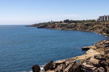Açık mavi gökyüzünün altında Guia deniz feneri olan engebeli kıyı şeridi.