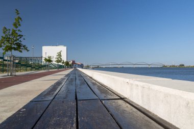 Boş bank ziyaretçileri rahatlamaya davet ediyor ve Tagus nehri manzarasının ve vila franca de xira köprüsünün tadını çıkarıyor.