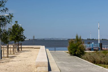 Alhandra, Portekiz 'deki bir parktan, Tagus nehri üzerindeki Vasco da Gama köprüsünün manzaralı manzarasında asfalt yol, ağaçlar ve sokak lambaları var.