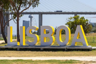 Arka planda güneşli bir günde Vasco da Gama Köprüsü ve sayısız otelle birlikte parktaki büyük Lisboa tabelası.