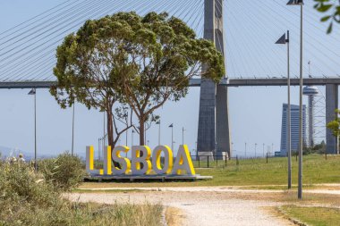 Ön planda Lisboa ve güneşli bir günün tadını çıkaran turistlerle Tagus Nehri üzerindeki Vasco da Gama Köprüsü manzarası