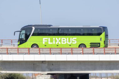 Şehir içi yeşil otobüs açık bir gökyüzünün altında köprüden geçiyor.