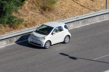 Güneşli bir günde beyaz Toyota Iq otoyolda araba sürüyor.