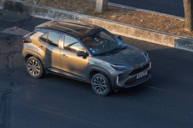 Modern Toyota Yaris, gün batımında asfalt yolda giderken melez bir araba kullanıyor.