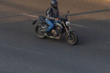 Kasklı ve koruyucu ceketli bisikletçi kaldırımlı yolda çağdaş motosiklet sürüyor.