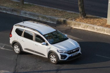 Şehir kavşağından geçen modern beyaz dacia koşucusu, tasarımını ve kentsel adaptasyonunu sergiliyor
