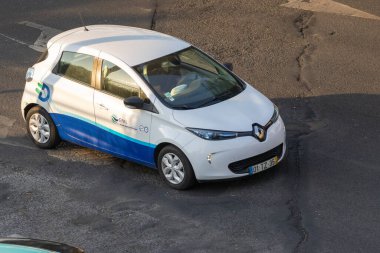 Ak Renault Zoe elektrikli arabası şehir ortamında asfalt yolda, sürdürülebilir ulaşımı teşvik ediyor.