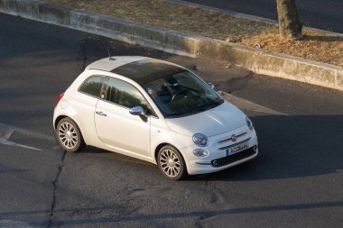 Siyah çatılı beyaz Fiat 500 bir asfalt yolda dönüyor.