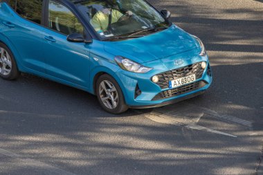 Mavi hyundai i10 otomobil şehir ortamında asfalt bir yolda ilerliyor