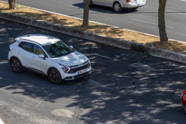 Kentsel bir ortamda asfalt bir yolda sürerken modern beyaz kia spor SUv, parlak tasarımını ve çağdaş özelliklerini sergiliyor