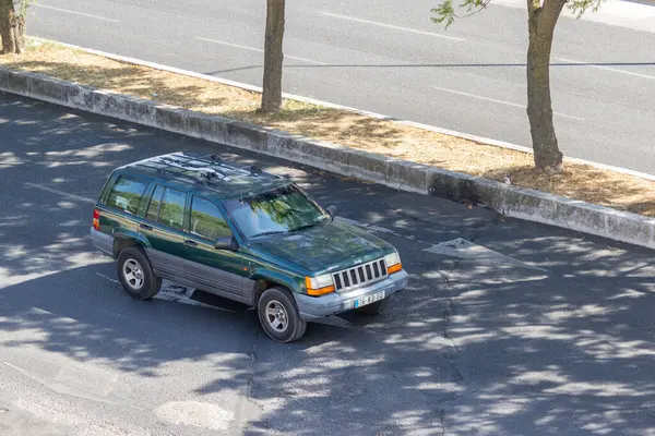 Ağaçların gölgesinin altında asfalt bir yolun kenarına park edilmiş yeşil bir cip.