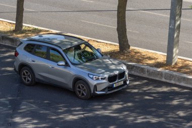 Çağdaş gümüş renkli BMW x1 kaldırım kenarına park edilmiş, içinde sürücü oturuyor.