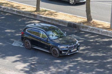 Modern siyah bmw x1 asfalt yolda giderken ağaçlar yere gölge düşürüyor.