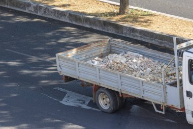 Asfalt yolda inşaat enkazı taşıyan küçük bir kamyon, kentsel ortamlarda atık yönetimi vurguluyor