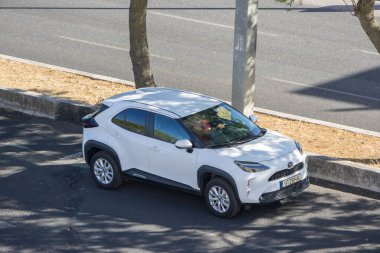 Modern beyaz toyota yaris yol kenarına park edilmiş, yaz güneşinin tadını çıkarıyor.