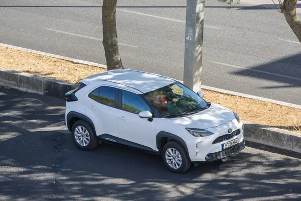 Modern beyaz toyota yaris yol kenarına park edilmiş, yaz güneşinin tadını çıkarıyor.